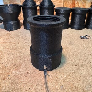 May include: Black textured metal objects, possibly for brewing or dispensing. The objects have a cylindrical or conical shape, with some featuring a spout and tubing. The items are arranged on a wooden surface.