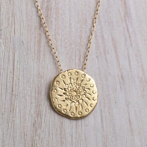 K&ouml;nnte beinhalten: Eine goldene Halskette mit einem runden Anh&auml;nger, der ein detailliertes Mandala-Design zeigt. Der Anh&auml;nger hat eine strukturierte Oberfl&auml;che und ein kreisf&ouml;rmiges Muster.