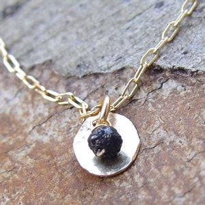 May include: A delicate gold chain necklace with a small round pendant featuring a black gemstone. The pendant is hammered and has a rustic, organic feel.