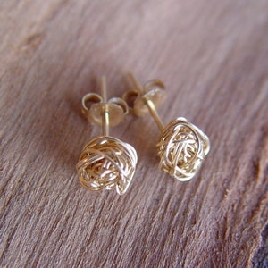 May include: A pair of gold wire earrings with a knotted design. The earrings are small and delicate.