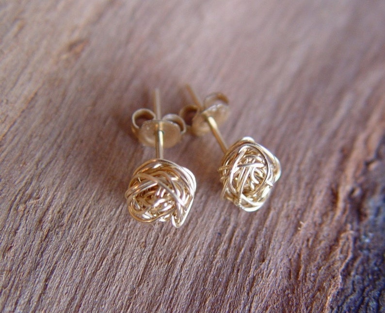 May include: A pair of gold wire earrings with a knotted design. The earrings are small and delicate.