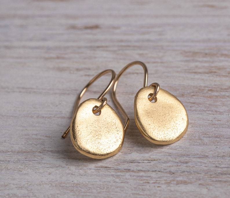 May include: A pair of gold-toned earrings with a teardrop shape. The earrings are made of a smooth, textured metal and have a simple, minimalist design.