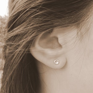May include: A close-up of a person's ear with a small, round, silver earring.