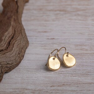 May include: A pair of gold-toned earrings with a textured, oval-shaped design. The earrings are hanging from a simple wire hook.