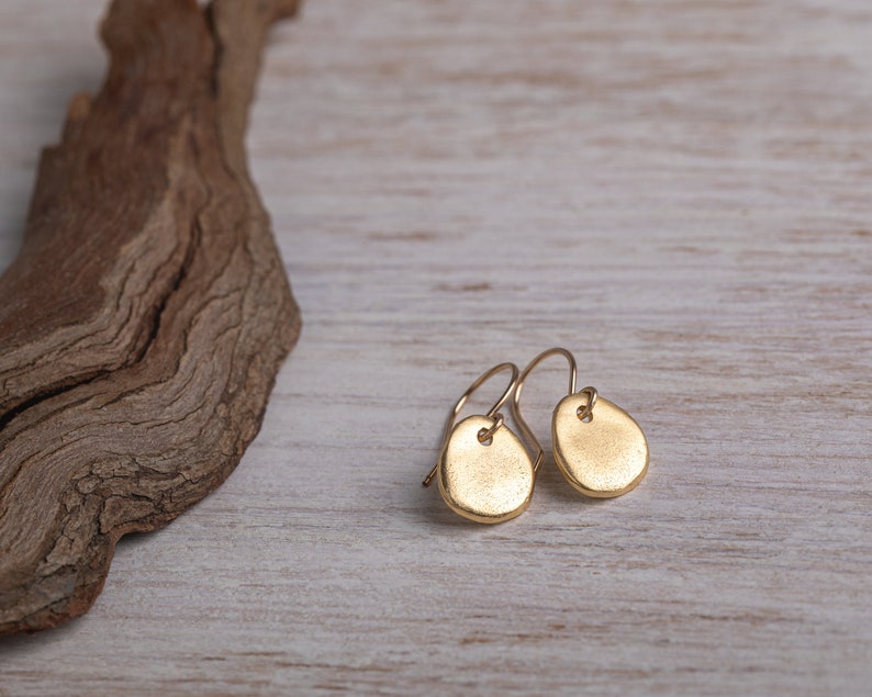 May include: A pair of gold-toned earrings with a textured, oval-shaped design. The earrings are hanging from a simple wire hook.