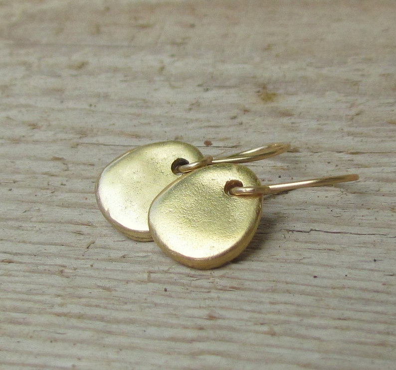 May include: A pair of gold-toned earrings with a simple, rounded shape. The earrings are made of metal and have a smooth, polished finish.