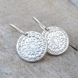 May include: A pair of silver earrings with a circular design. The earrings have a delicate, intricate pattern and a simple hook closure.