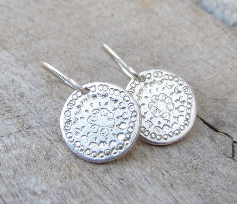 May include: A pair of silver earrings with a circular design. The earrings have a delicate, intricate pattern and a simple hook closure.
