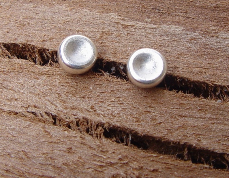 May include: A pair of silver stud earrings with a slightly domed shape.