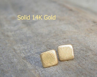 May include: A pair of small, square-shaped earrings made of solid 14K gold. The earrings have a brushed finish and are a light gold color.