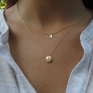 Op de afbeelding: Een gouden ketting met twee delicate kettingen en twee ronde hangers. De hangers zijn getextureerd en hebben een gehamerde afwerking.
