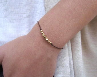 May include: A simple brown string bracelet with a row of gold beads.