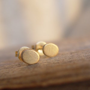 May include: A pair of gold-toned stud earrings with a circular design. The earrings are small and delicate, and they have a brushed finish.