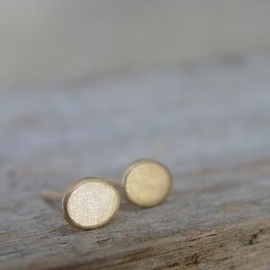 May include: A pair of small, round, gold-colored earrings. The earrings are simple and minimalist in design.