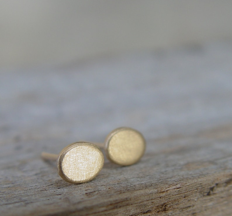 May include: A pair of small, round, gold-colored earrings. The earrings are simple and minimalist in design.