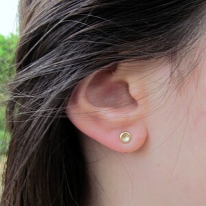 May include: A close-up of a person's ear with a small, round, gold earring. The earring has a smooth, shiny surface.