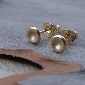 May include: A pair of gold stud earrings with a slightly rounded, slightly concave, brushed finish.