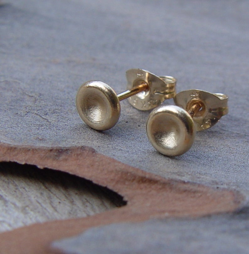 May include: A pair of gold stud earrings with a slightly rounded, slightly concave, brushed finish.