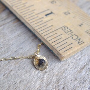 May include: A gold chain necklace with a small, round pendant. The pendant is made of gold and has a black stone in the center.