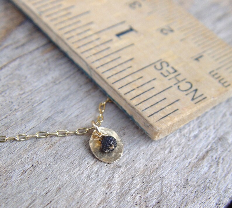 May include: A gold chain necklace with a small, round pendant. The pendant is made of gold and has a black stone in the center.