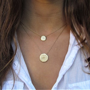 K&ouml;nnte beinhalten: Zwei goldene Halsketten mit runden Anh&auml;ngern. Der gr&ouml;&szlig;ere Anh&auml;nger hat ein detailliertes Design und der kleinere Anh&auml;nger ist glatt.
