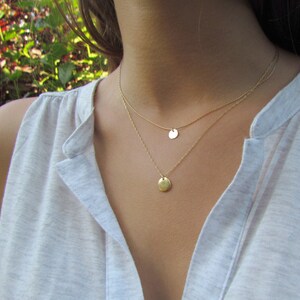Op de afbeelding: Een gouden ketting met twee ronde hangers. De ketting is gelaagd en de hangers zijn van verschillende grootte.