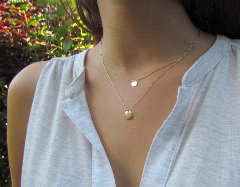 Op de afbeelding: Een gouden ketting met twee ronde hangers. De ketting is gelaagd en de hangers zijn van verschillende grootte.