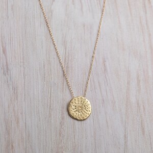 K&ouml;nnte beinhalten: Eine goldene Halskette mit einem runden Anh&auml;nger, der ein detailliertes Sonnenmotiv zeigt.