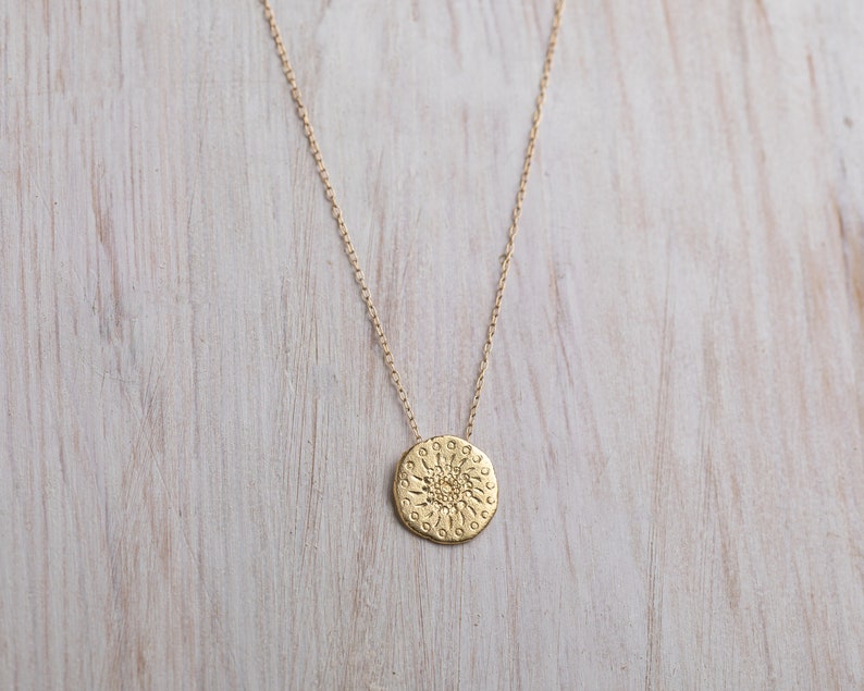 K&ouml;nnte beinhalten: Eine goldene Halskette mit einem runden Anh&auml;nger, der ein detailliertes Sonnenmotiv zeigt.