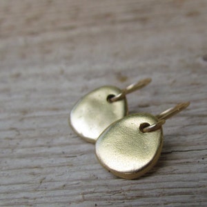 May include: A pair of gold-toned earrings with a simple, rounded shape. The earrings are made of metal and have a smooth, polished finish.