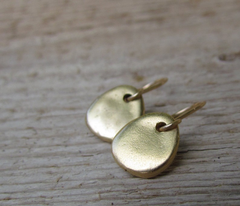 May include: A pair of gold-toned earrings with a simple, rounded shape. The earrings are made of metal and have a smooth, polished finish.