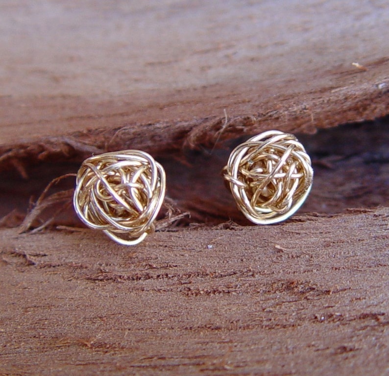 May include: A pair of gold wire earrings with a knotted design. The earrings are small and delicate, and they would make a great gift for a friend or loved one.