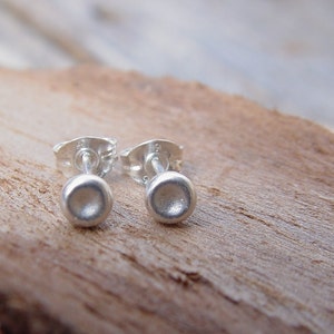 May include: A pair of silver stud earrings with a round, slightly domed shape. The earrings are simple and minimalist.
