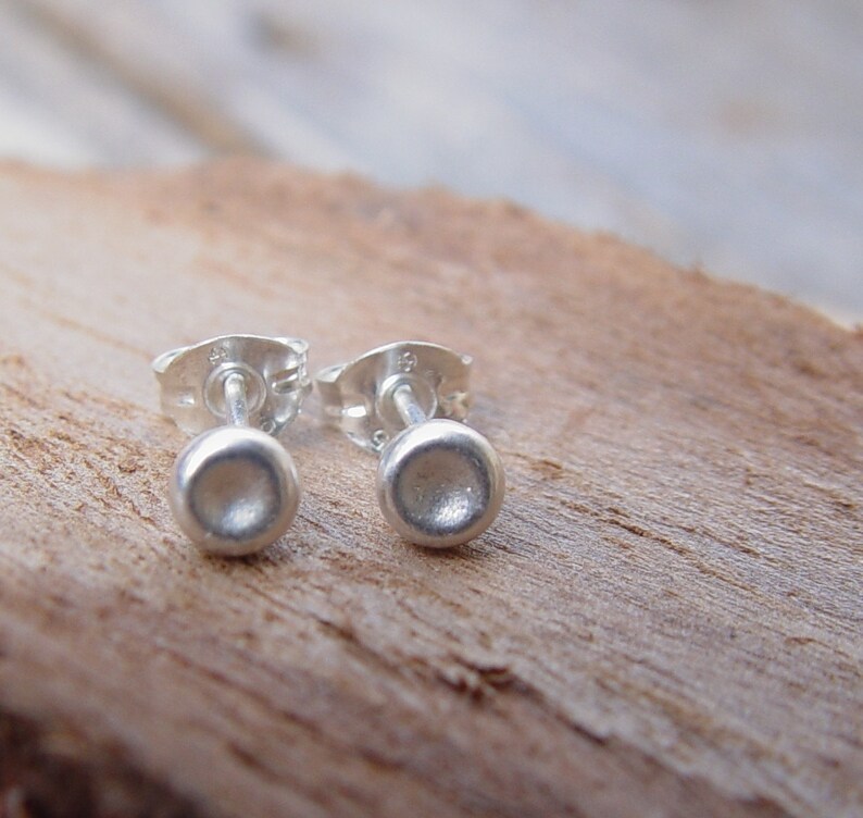 May include: A pair of silver stud earrings with a round, slightly domed shape. The earrings are simple and minimalist.