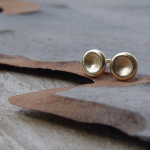 May include: A pair of gold-toned stud earrings with a round, slightly concave design.