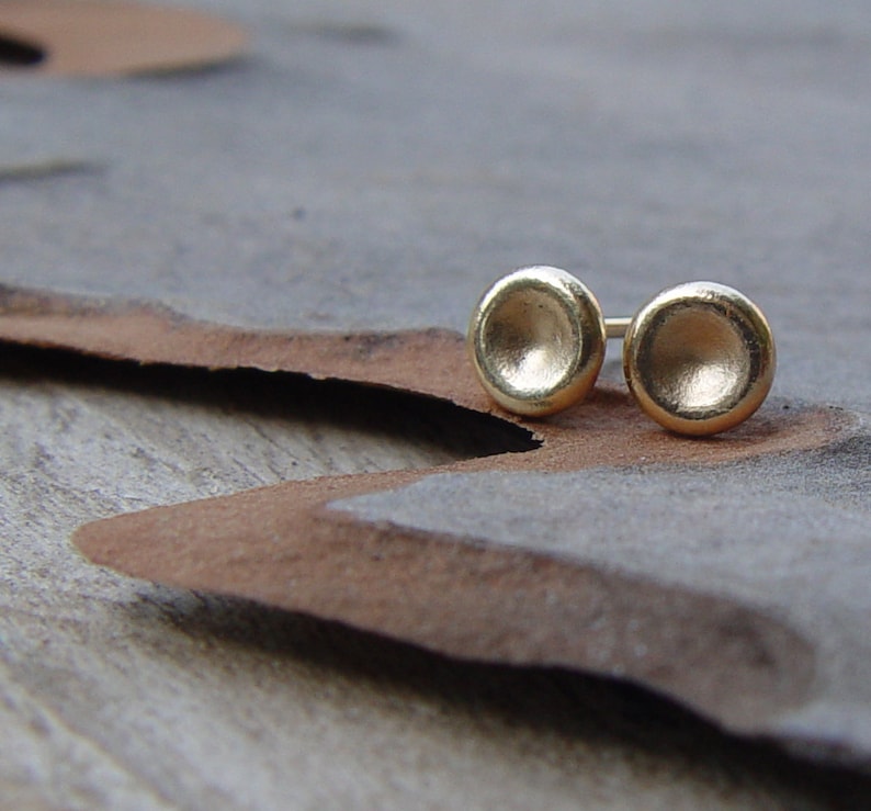 May include: A pair of gold-toned stud earrings with a round, slightly concave design.