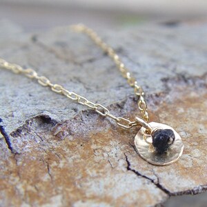 May include: A delicate gold chain necklace with a small, round pendant featuring a black gemstone. The pendant is textured and has a hammered finish.