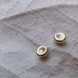May include: Two small, round, silver-colored earrings. The earrings are slightly concave and have a smooth, polished finish.