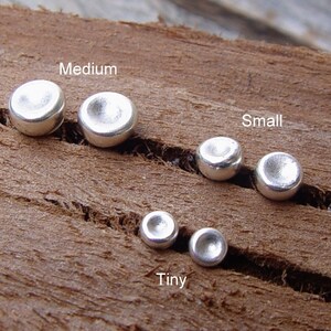 Op de afbeelding: Vijf zilveren metalen schijven in verschillende maten, gelabeld met "Tiny", "Small" en "Medium".