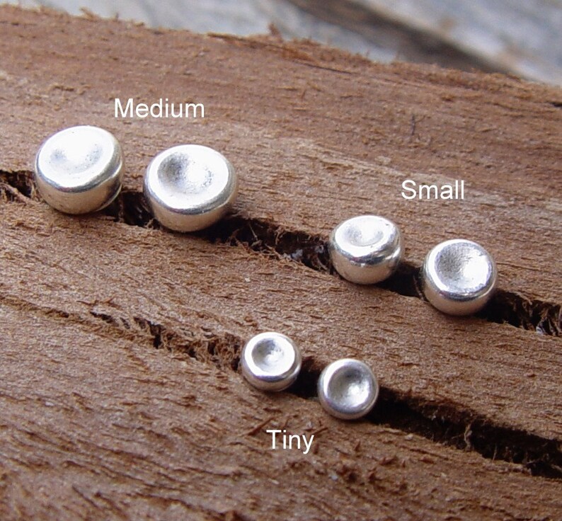 Op de afbeelding: Vijf zilveren metalen schijven in verschillende maten, gelabeld met "Tiny", "Small" en "Medium".