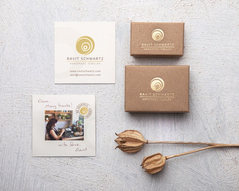 May include: A brown cardboard box with a gold logo that says "Ravit Schwartz Handmade Jewelry". The box is sitting on a white surface with a handwritten note that says "Dear, Many thanks! With love, Ravit".