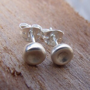 Op de afbeelding: Een paar zilveren oorbel studs met een glad, afgerond ontwerp. De oorbellen zijn gemaakt van sterling zilver en hebben een post-back sluiting.