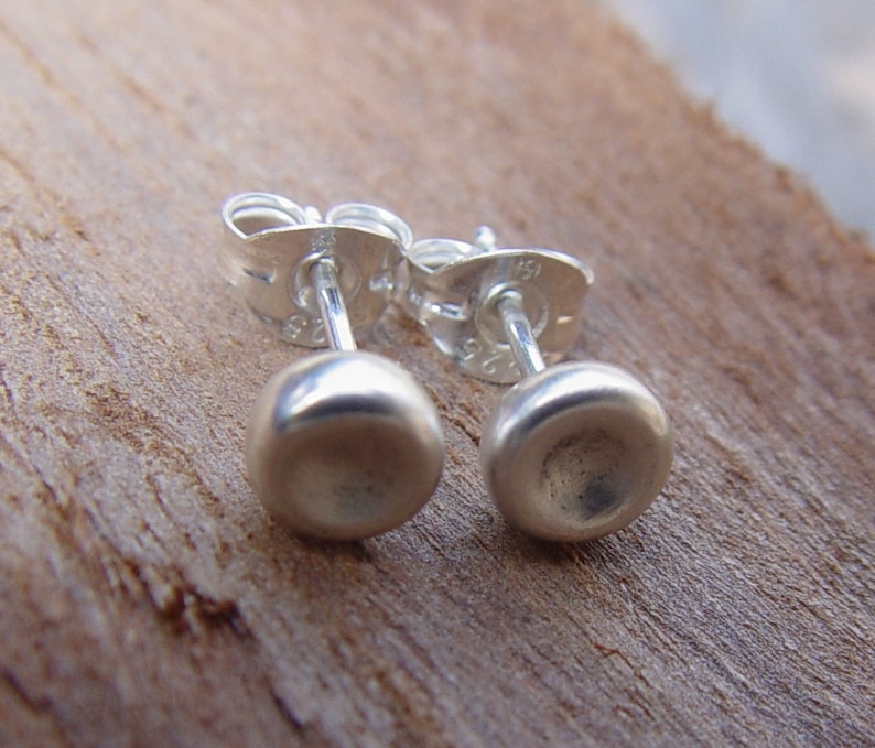 Op de afbeelding: Een paar zilveren oorbel studs met een glad, afgerond ontwerp. De oorbellen zijn gemaakt van sterling zilver en hebben een post-back sluiting.