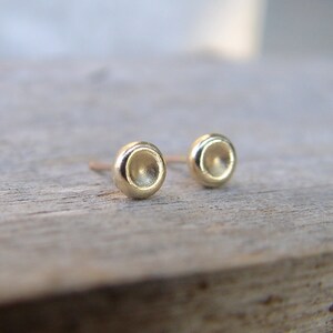 May include: A pair of small, gold, round stud earrings. The earrings have a slightly concave, or indented, surface.