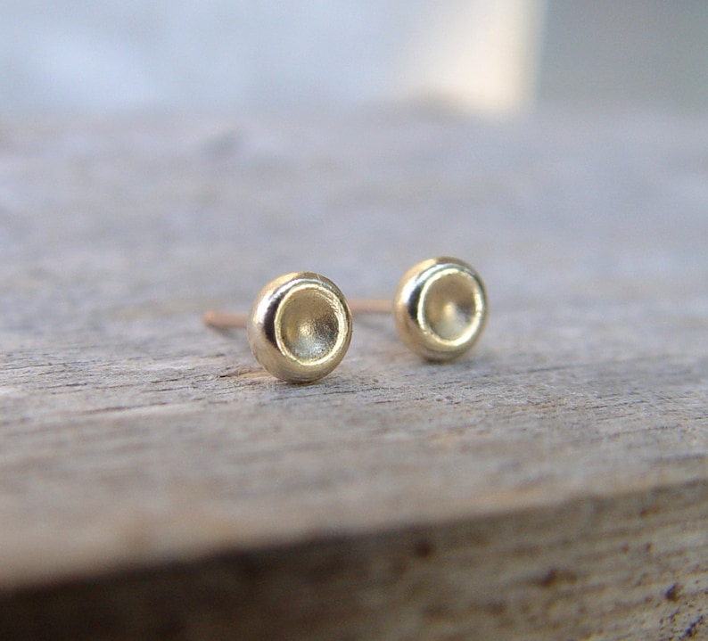 May include: A pair of small, gold, round stud earrings. The earrings have a slightly concave, or indented, surface.