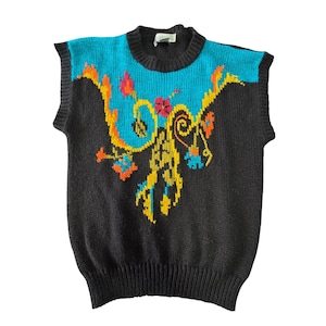 May include: A sleeveless sweater in dark gray with a turquoise yoke and a colorful floral design. The design features yellow, orange, and pink flowers and swirls. The sweater has a ribbed neckline and hem.