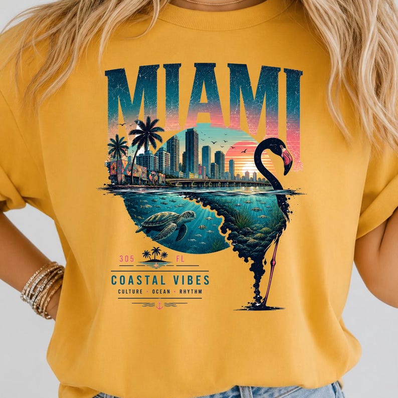 May include: A mustard yellow t-shirt featuring a graphic print of the Miami skyline at sunset, a sea turtle swimming underwater, and a flamingo silhouette. The text reads MIAMI, 305 FL, COASTAL VIBES, CULTURE, OCEAN, RHYTHM.