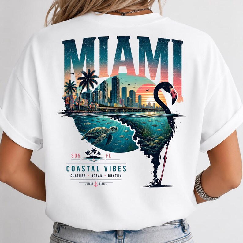 May include: A white t-shirt featuring a graphic on the back with the text MIAMI in large letters above a city skyline, a sunset, a sea turtle swimming underwater, and a flamingo silhouette. Below is the text 305 FL COASTAL VIBES CULTURE OCEAN RHYTHM.