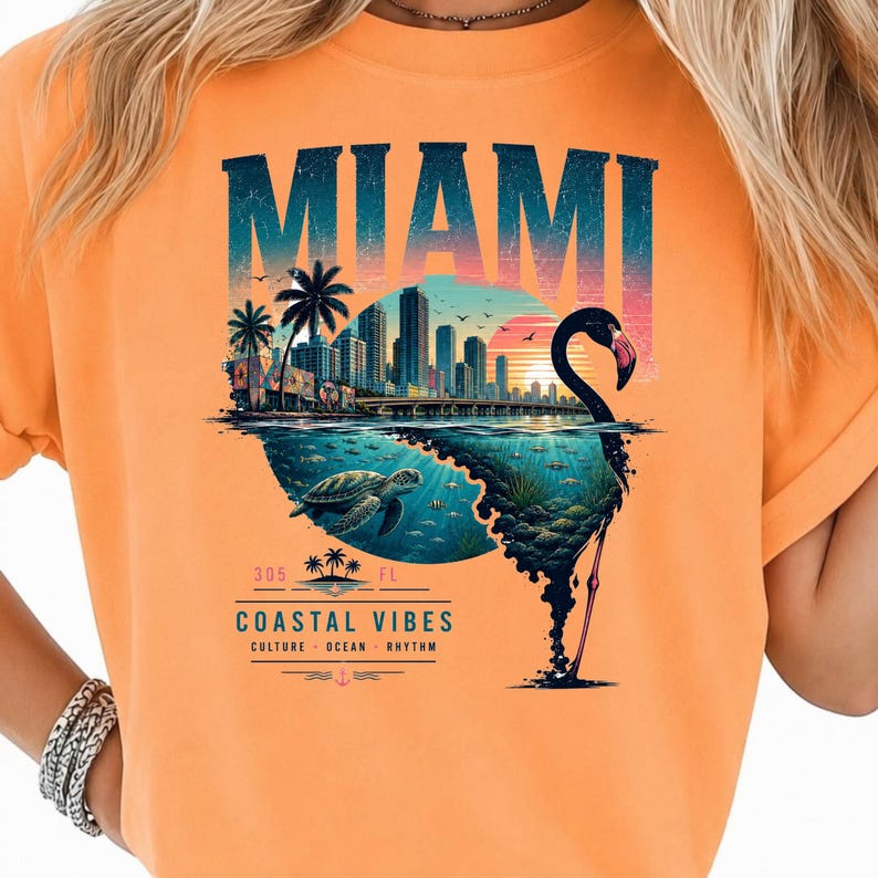 May include: An orange t-shirt featuring a graphic print with the text MIAMI at the top. The design includes a city skyline, a sunset, a sea turtle swimming underwater, and a large flamingo silhouette. Below, the text reads 305 FL COASTAL VIBES.