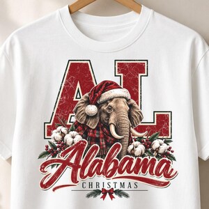 Könnte beinhalten: Ein weißes T-Shirt mit einer Grafik eines Elefanten, der eine Weihnachtsmütze und einen rot karierten Schal trägt. Das Design zeigt die großen roten Buchstaben AL, das Wort Alabama in roter Schreibschrift, CHRISTMAS, Baumwolle und rote Beeren.